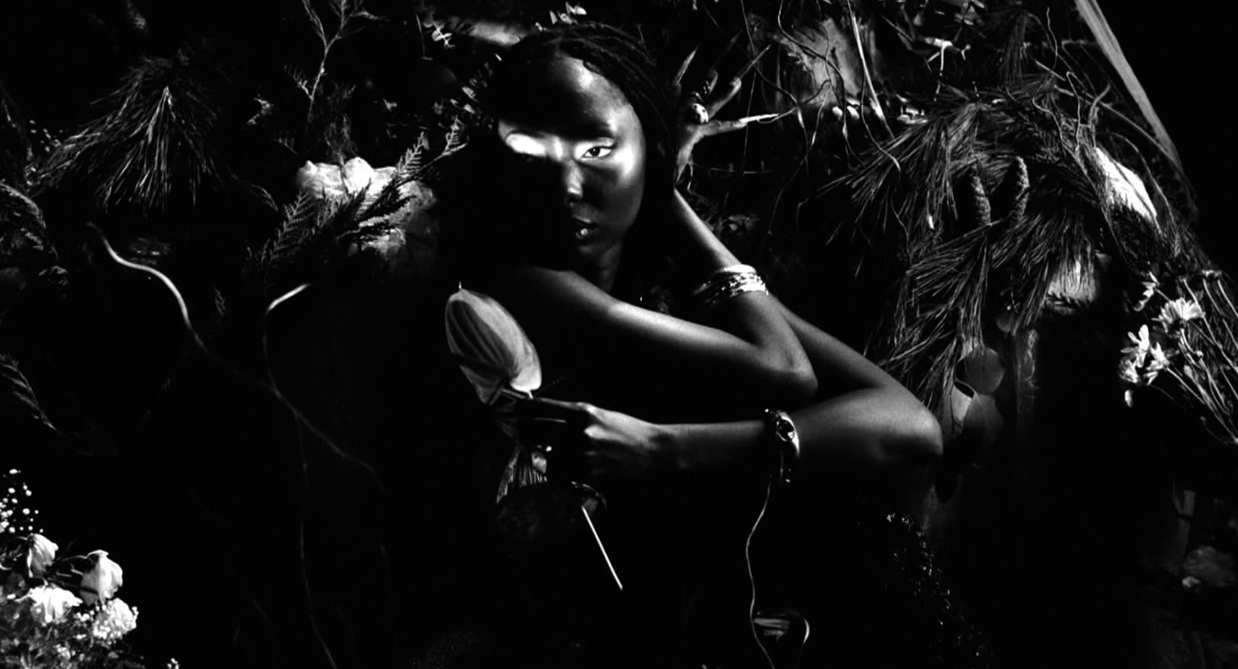 Black and white shot of a model with deep skin holding a flower with a beam of light cascading over her eyes.